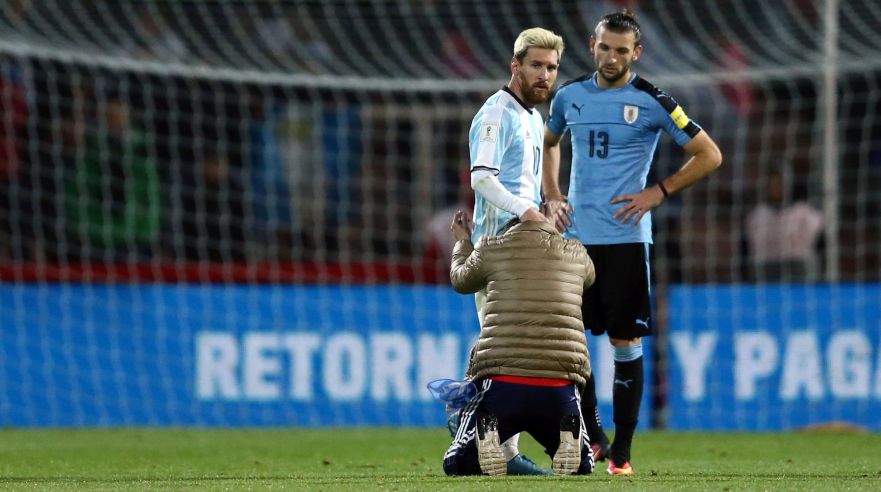 Football Soccer - World Cup 2018 Qualifiers - Argentina v Uruguay - Estadio Malvinas Argentinas, Mendoza, Argentina - 01/09/16 - A fan who jumped onto the field kneels to touch Argentina's Lionel Messi while Uruguay's Gaston Silva (R) looks on. REUTERS/Marcos Brindicci