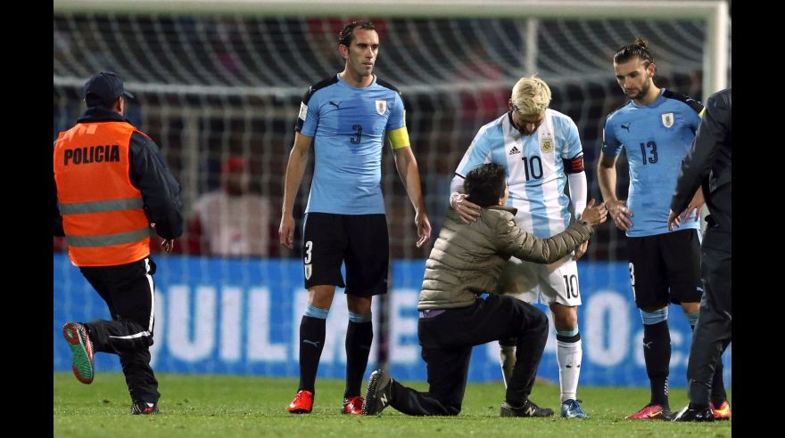 Football Soccer - World Cup 2018 Qualifiers - Argentina v Uruguay - Estadio Malvinas Argentinas, Mendoza, Argentina - 01/09/16 - A fan who jumped onto the field kneels to touch Argentina's Lionel Messi while Uruguay's Gaston Silva (R) and Diego Godin look on. REUTERS/Marcos Brindicci